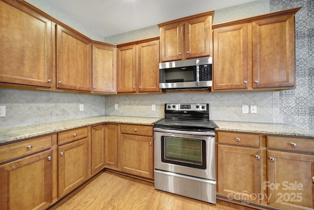 kitchen with light stone countertops, decorative backsplash, light wood-style flooring, appliances with stainless steel finishes, and brown cabinets