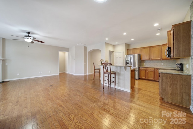 kitchen with brown cabinets, a breakfast bar, stainless steel appliances, light wood finished floors, and decorative backsplash