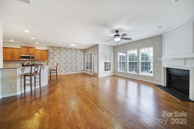 unfurnished living room featuring a ceiling fan, baseboards, recessed lighting, hardwood / wood-style flooring, and a glass covered fireplace