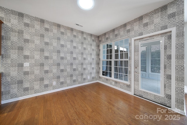 spare room featuring visible vents, wallpapered walls, baseboards, and wood finished floors