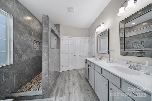 bathroom with double vanity, a walk in shower, wood finished floors, and a sink