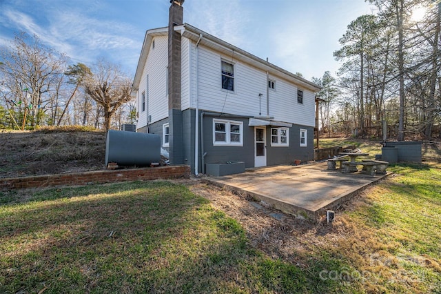 rear view of property with a chimney, a patio area, a lawn, and heating fuel