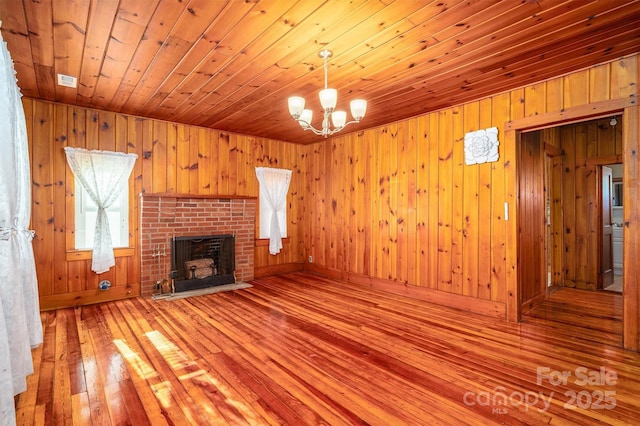 unfurnished living room featuring a notable chandelier, wood walls, a fireplace, wood ceiling, and light wood-type flooring