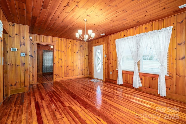 unfurnished room featuring wooden walls, wooden ceiling, wood finished floors, and an inviting chandelier