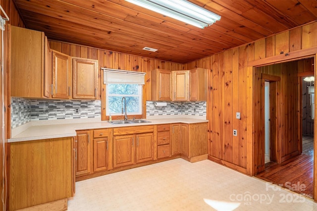 kitchen featuring light countertops, backsplash, brown cabinetry, wood ceiling, and a sink