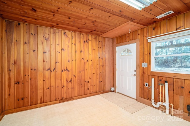 foyer entrance featuring wood ceiling, light floors, visible vents, and wooden walls