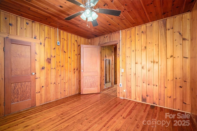 unfurnished room featuring wooden ceiling, light wood-style flooring, a ceiling fan, and wood walls