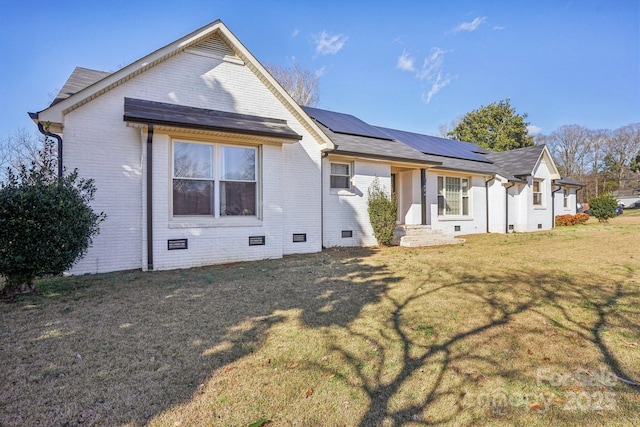 back of house featuring crawl space, brick siding, a lawn, and solar panels