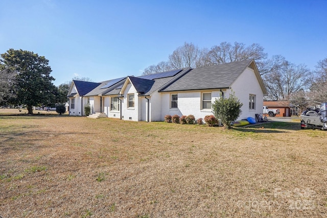 view of front of property with a front yard, roof mounted solar panels, and brick siding