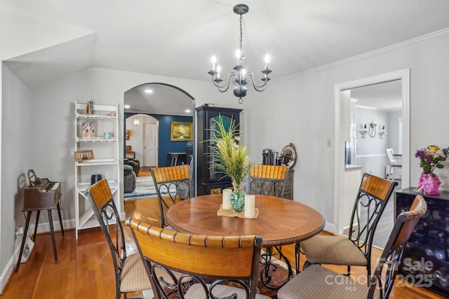 dining space with arched walkways, crown molding, lofted ceiling, wood finished floors, and baseboards