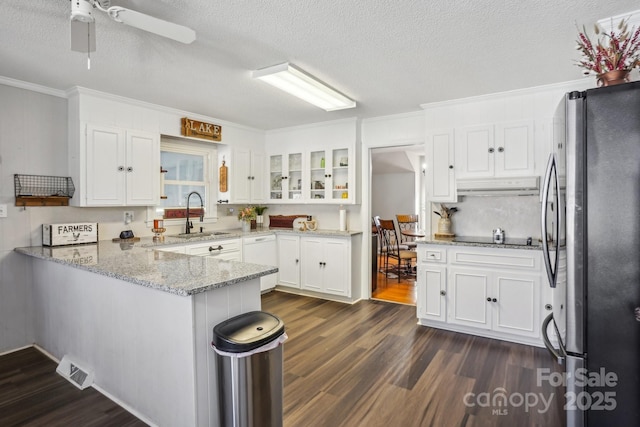 kitchen with white cabinets, glass insert cabinets, freestanding refrigerator, a peninsula, and a sink