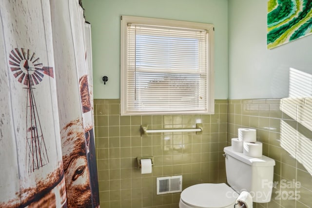 full bathroom with a wainscoted wall, visible vents, tile walls, and toilet