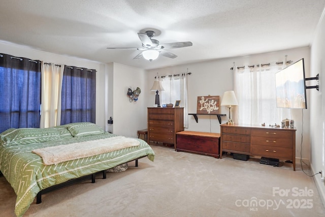 bedroom with a ceiling fan, multiple windows, light carpet, and a textured ceiling