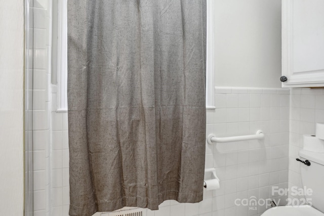 bathroom featuring toilet, a wainscoted wall, and tile walls