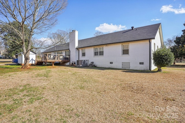 back of house featuring brick siding, a yard, crawl space, a storage unit, and a chimney