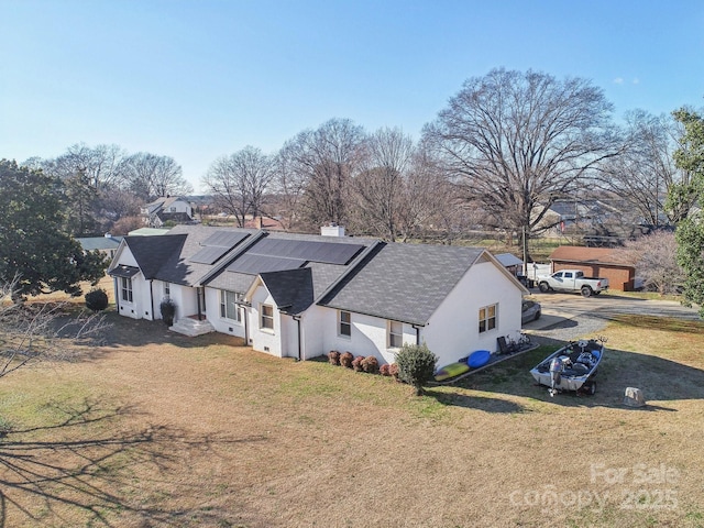 exterior space with a shingled roof, a residential view, roof mounted solar panels, a front lawn, and stucco siding