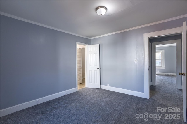 spare room with dark colored carpet, crown molding, and baseboards