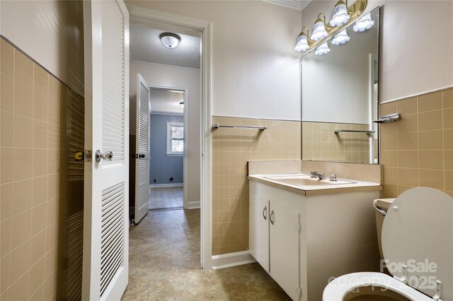 half bath with a textured ceiling, toilet, vanity, tile walls, and wainscoting