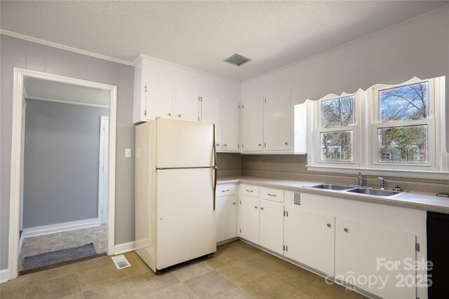 kitchen with crown molding, light countertops, freestanding refrigerator, white cabinets, and a sink