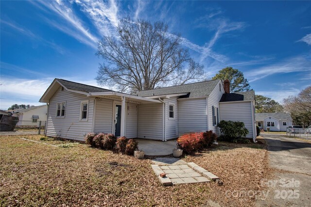 ranch-style home with a chimney, fence, and roof with shingles