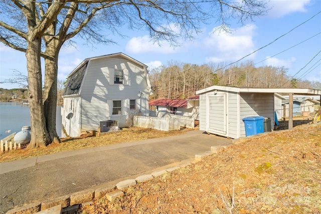 view of side of home with cooling unit, a water view, fence, and a gambrel roof