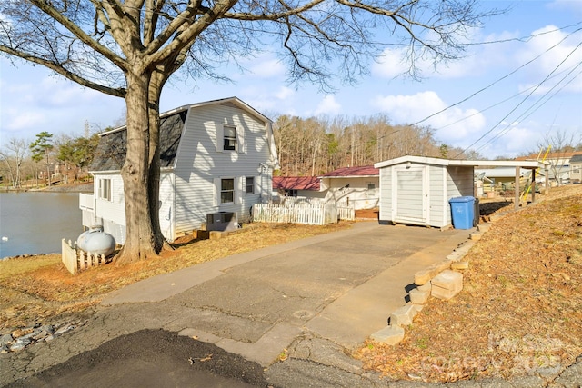 view of property exterior with cooling unit, a water view, fence, and a gambrel roof