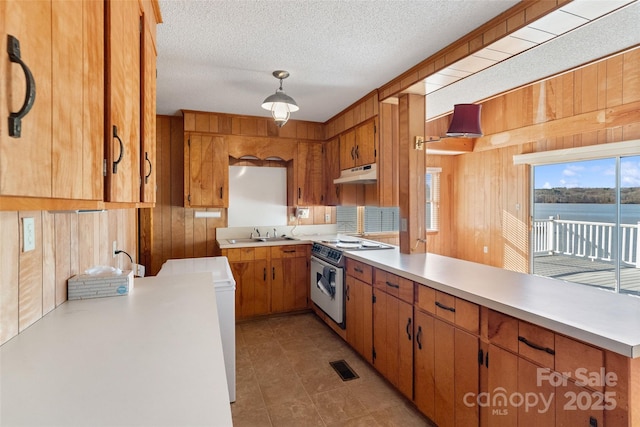 kitchen with white range with electric cooktop, light countertops, brown cabinetry, wooden walls, and under cabinet range hood