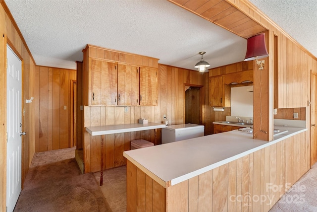 kitchen featuring a textured ceiling, light colored carpet, a peninsula, wood walls, and light countertops