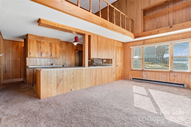 kitchen featuring a baseboard radiator, a peninsula, light countertops, carpet floors, and wood walls