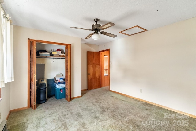 unfurnished bedroom with a closet, light colored carpet, a ceiling fan, attic access, and baseboards