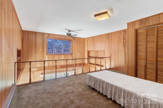 bedroom with a baseboard heating unit, wood walls, dark carpet, and a textured ceiling