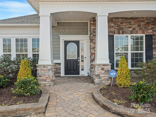 doorway to property with stone siding, a shingled roof, and a porch