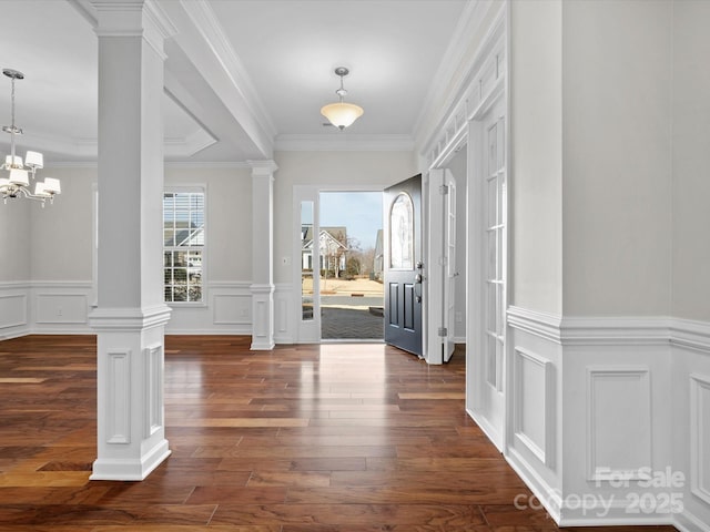 foyer entrance with ornamental molding, a chandelier, dark wood finished floors, and ornate columns