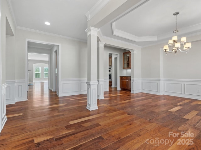 unfurnished dining area with decorative columns, dark wood-style floors, crown molding, a decorative wall, and a notable chandelier