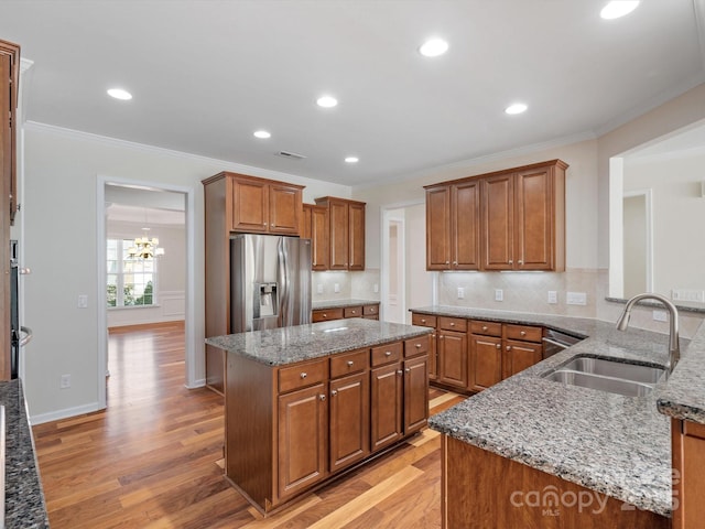 kitchen featuring stone counters, brown cabinets, stainless steel refrigerator with ice dispenser, light wood-style floors, and a sink