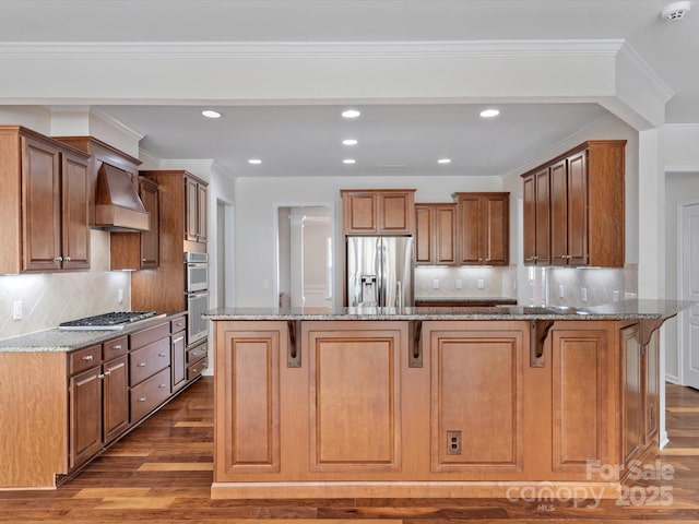 kitchen with wood finished floors, appliances with stainless steel finishes, light stone countertops, a kitchen bar, and custom range hood