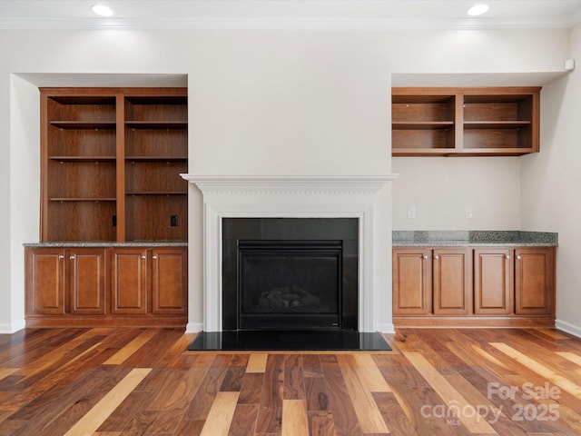 unfurnished living room featuring dark wood-style flooring, recessed lighting, a fireplace with flush hearth, ornamental molding, and baseboards