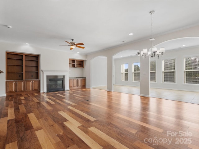 unfurnished living room featuring ceiling fan with notable chandelier, wood finished floors, plenty of natural light, and a glass covered fireplace