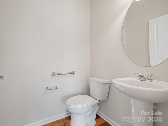 half bath with a sink, toilet, baseboards, and wood finished floors