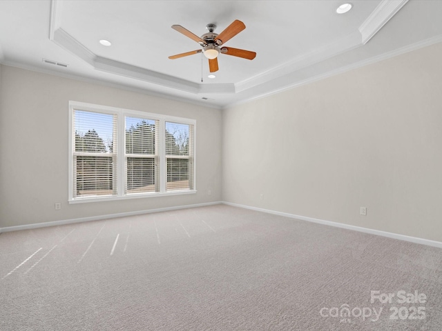 carpeted empty room featuring visible vents, baseboards, ceiling fan, a tray ceiling, and crown molding