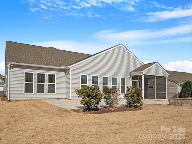 rear view of property featuring a patio area, a shingled roof, and a sunroom