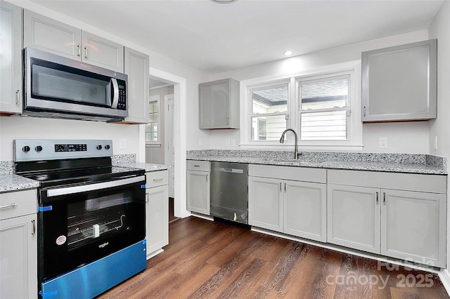 kitchen with stainless steel appliances, dark wood-style flooring, a sink, gray cabinets, and light stone countertops