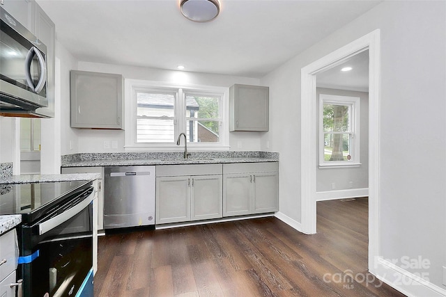 kitchen with stainless steel appliances, baseboards, gray cabinets, light stone countertops, and dark wood finished floors