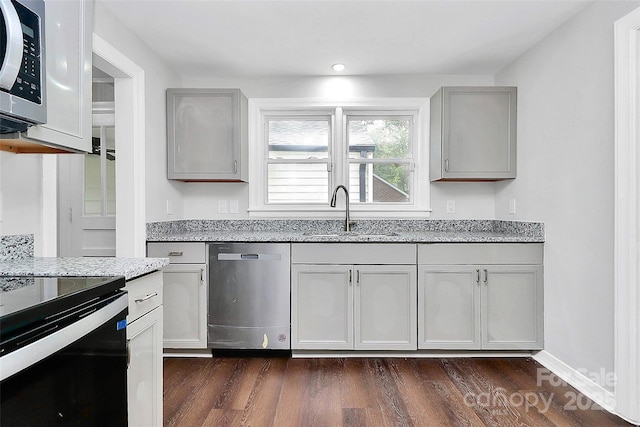 kitchen featuring stainless steel appliances, light stone counters, gray cabinets, and a sink