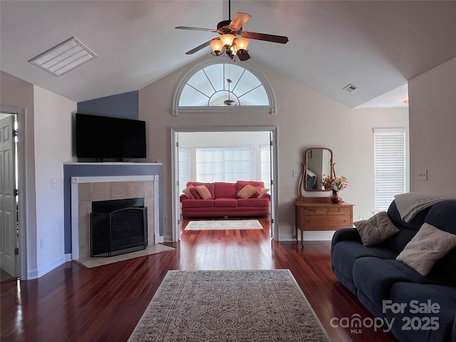 living area with ceiling fan, a fireplace, visible vents, vaulted ceiling, and wood-type flooring