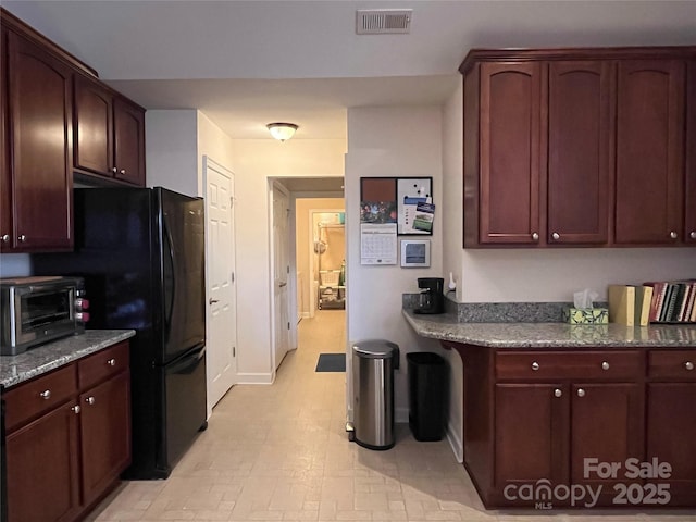 kitchen with freestanding refrigerator, a toaster, visible vents, and dark stone countertops