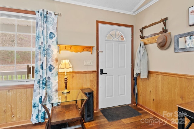 foyer entrance with a textured ceiling, a wainscoted wall, dark wood-style flooring, wood walls, and ornamental molding