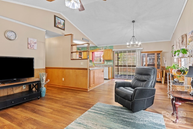 living area featuring lofted ceiling, ceiling fan with notable chandelier, light wood-style floors, ornamental molding, and wainscoting