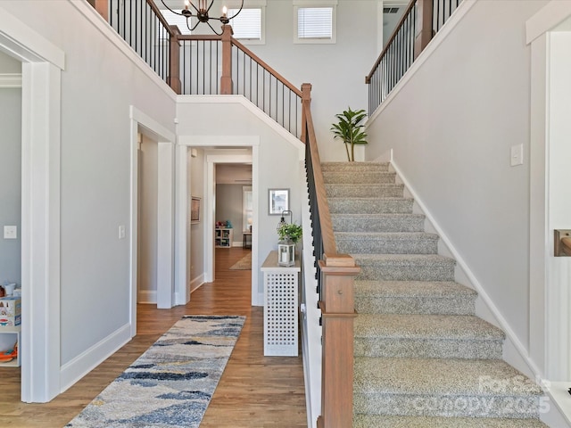 staircase with a chandelier, baseboards, a high ceiling, and wood finished floors