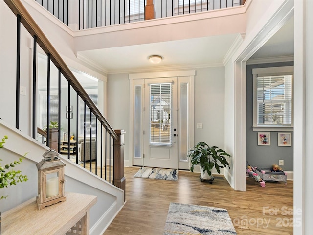 foyer entrance featuring crown molding, a high ceiling, wood finished floors, baseboards, and stairs